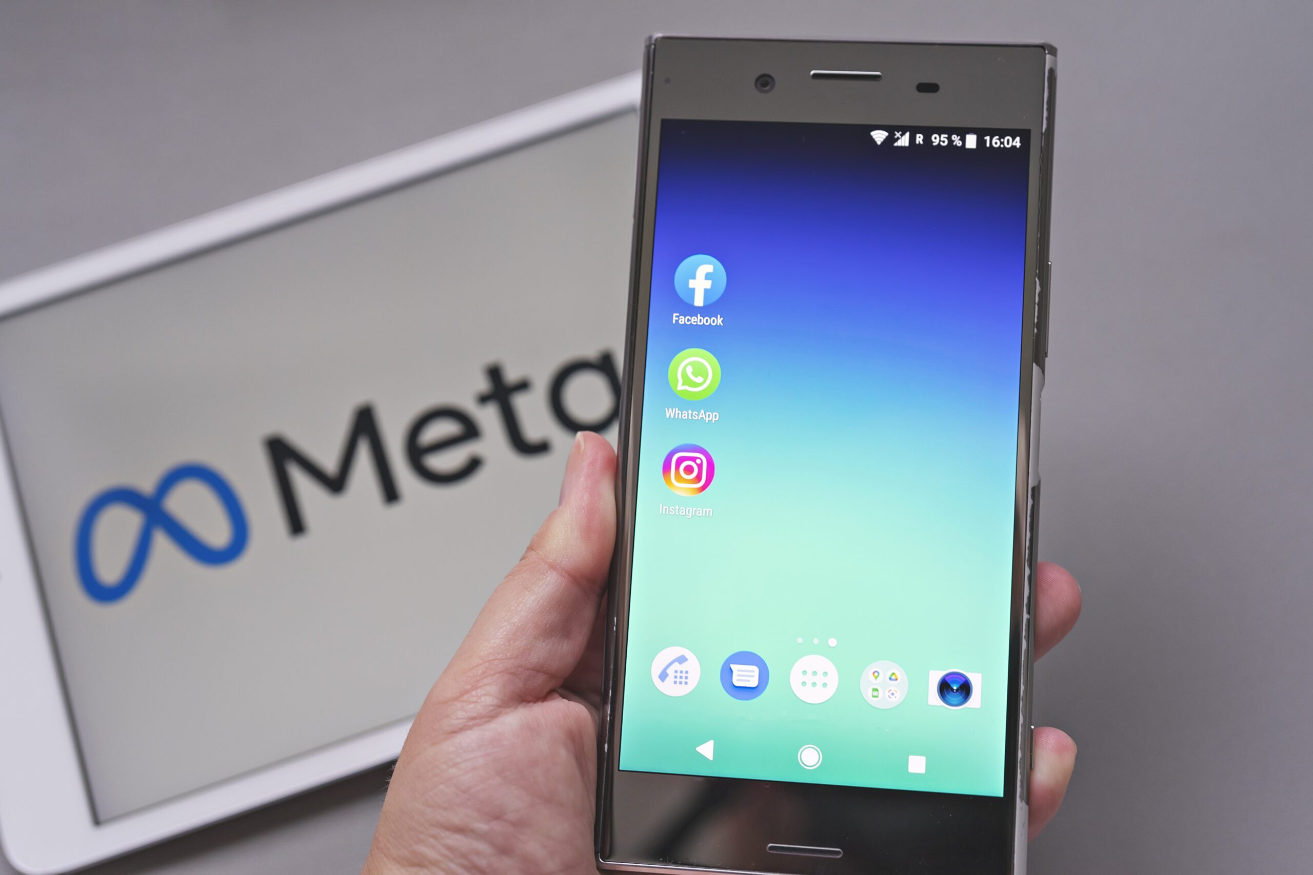 Smartphone display with logo of Facebook, WhatsApp and Instagram apps in hand in against blurred META logotype on white background tablet monitor